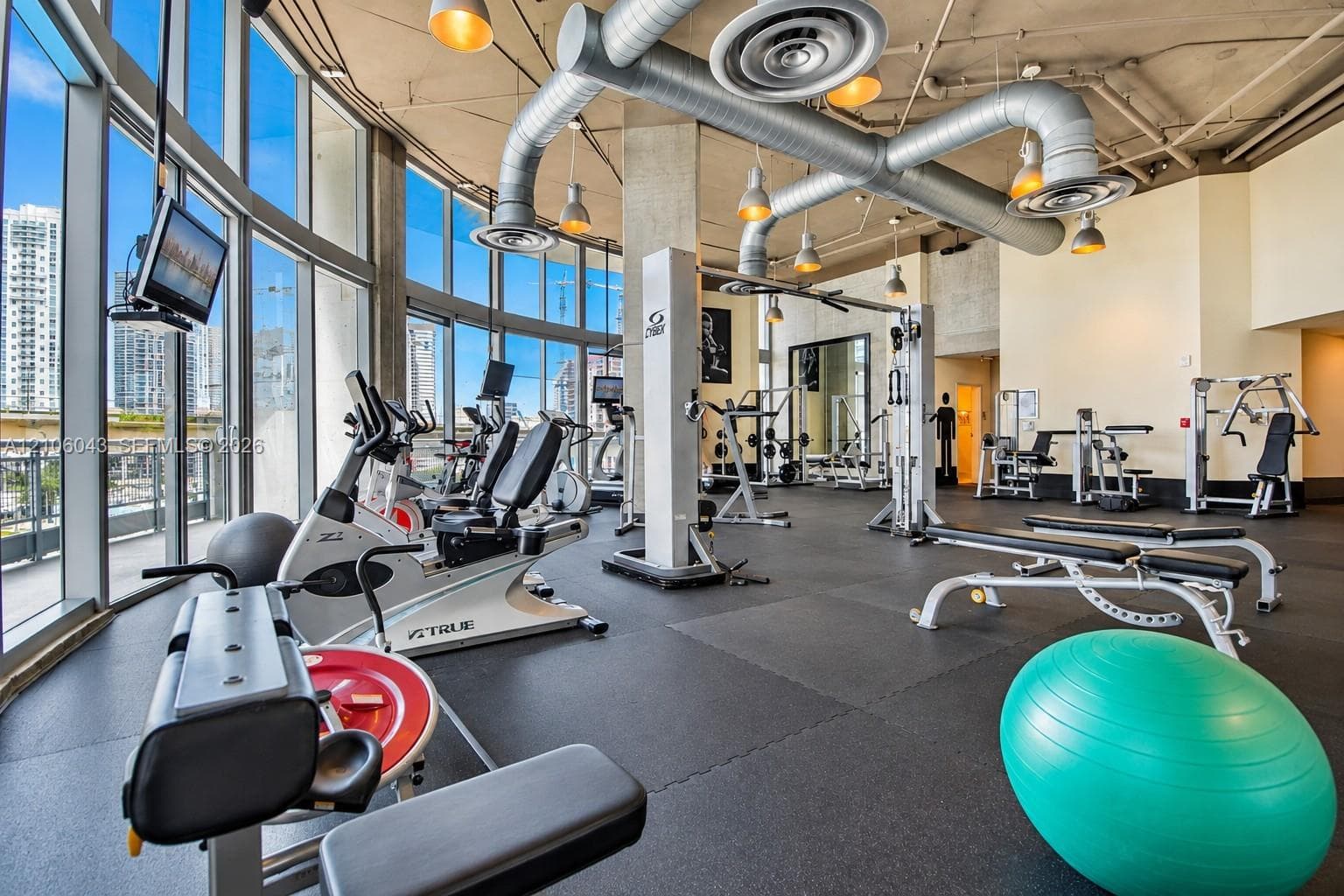 Fitness center featuring floor-to-ceiling windows, exposed concrete ceilings, industrial-style ductwork, and rubberized flooring