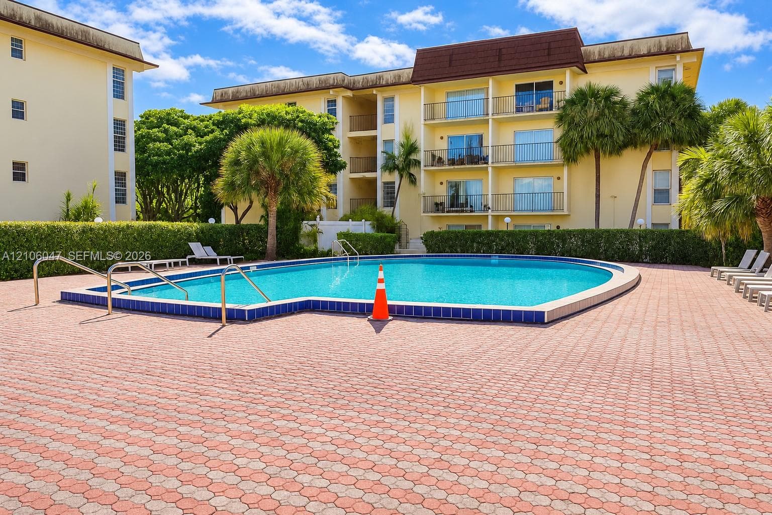 In-ground swimming pool with tile surround, paver-stone decking, multi-story building exterior, and mature palm trees