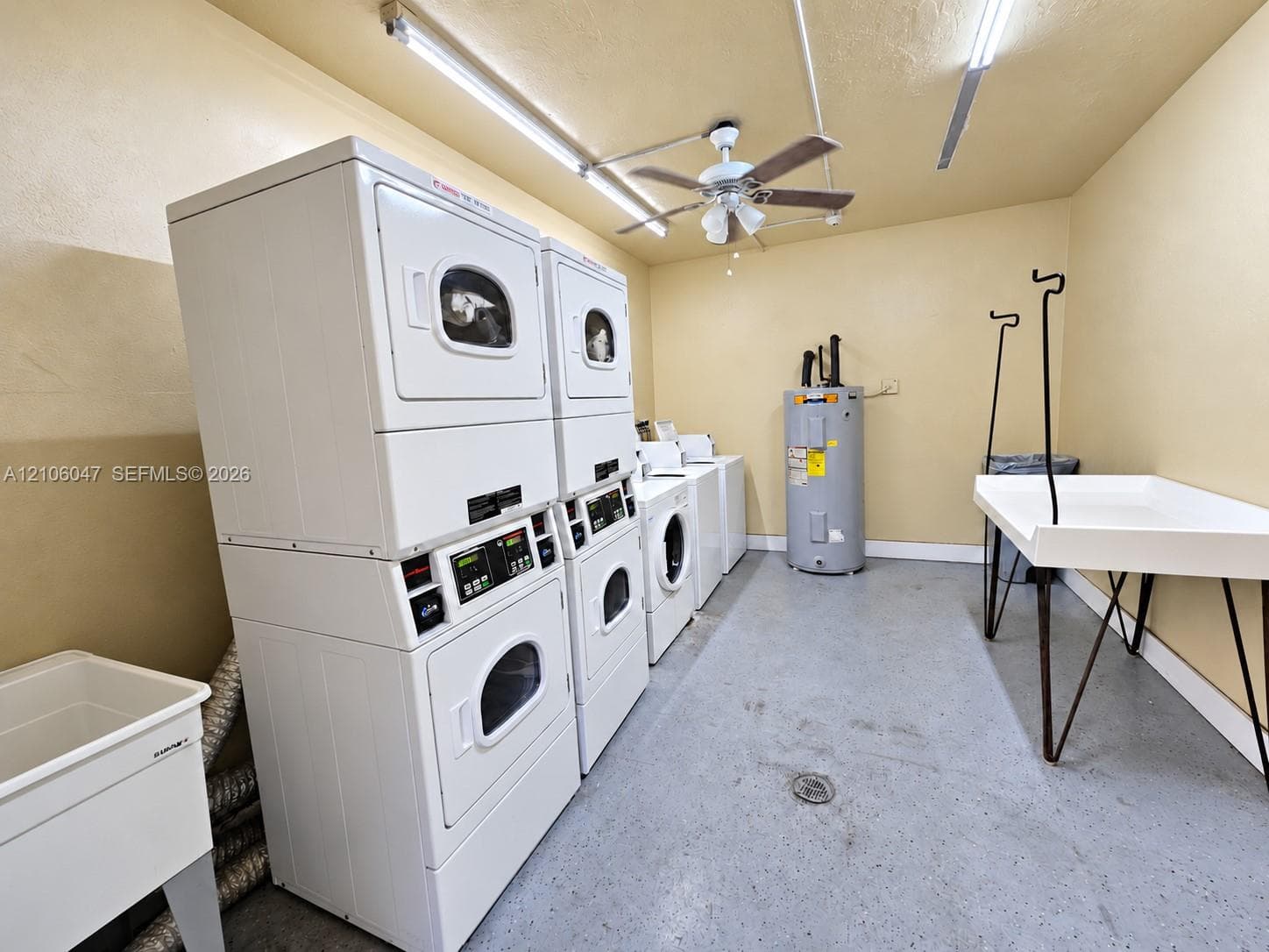 Utility area featuring multi-unit laundry appliances, a built-in utility sink, a tank-style water heater, and a ceiling-mounted fan with integrated light fixtures