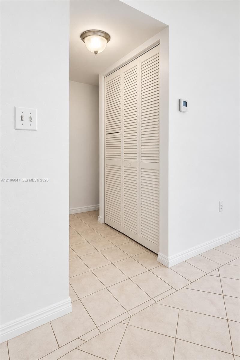 Tile flooring set on a diagonal pattern, closet featuring white louvered bi-fold doors, and a ceiling-mounted flush-mount light fixture