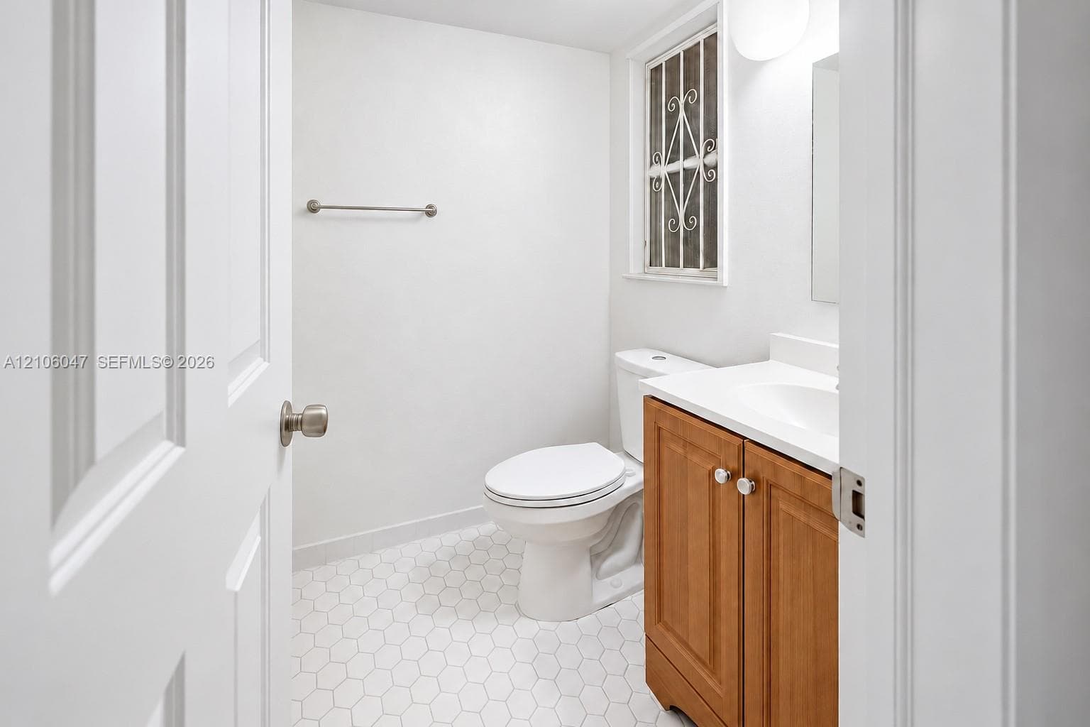 Bathroom featuring hexagon tile flooring, wood-finish vanity with a white countertop, wall-mounted hardware, and a window with decorative security bars