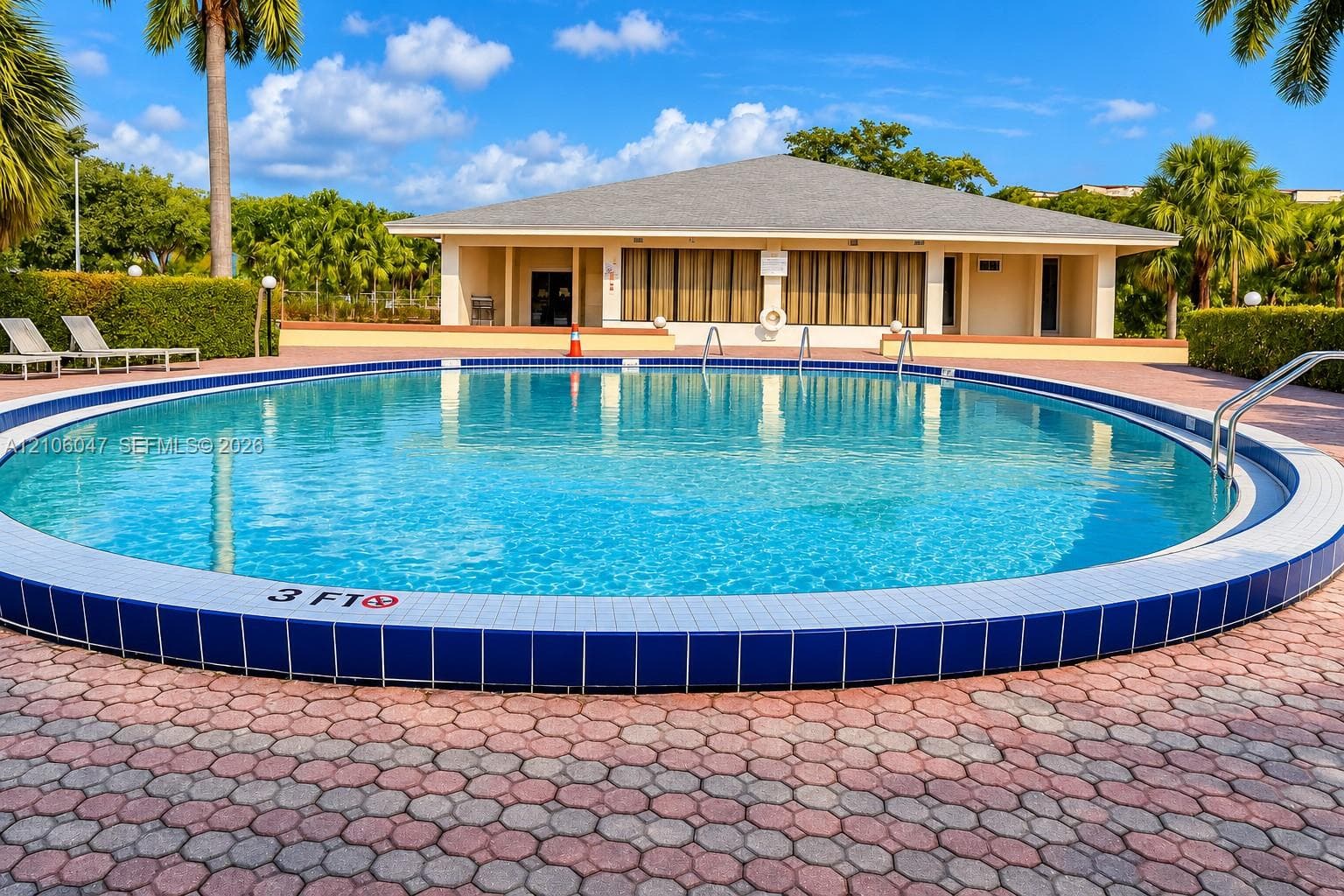 Circular swimming pool featuring a tiled edge, metal handrails, and a surrounding paver deck