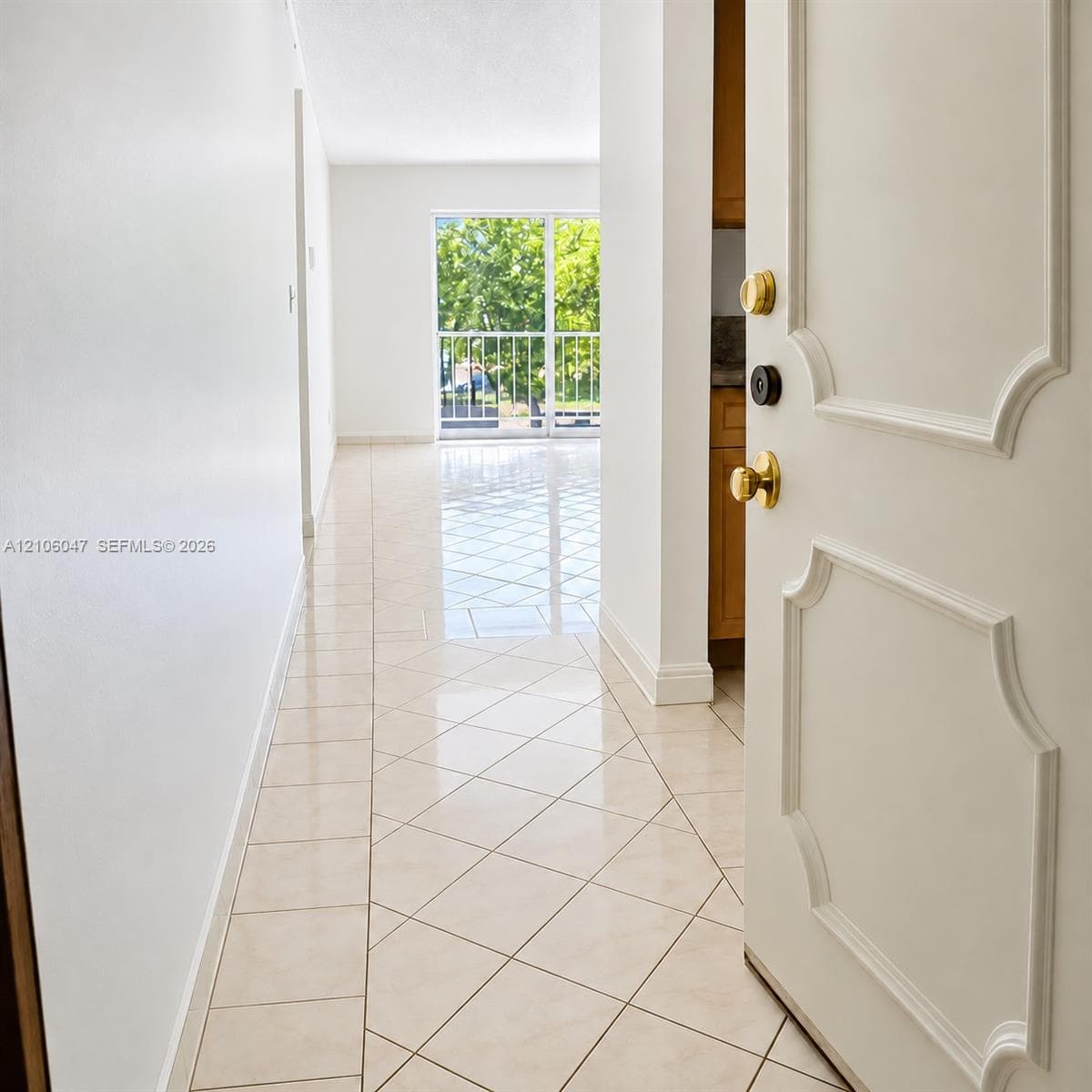 Entryway featuring tile flooring laid in a diamond pattern, white interior walls, a paneled door with polished brass hardware, and a sliding glass door with a metal balcony railing