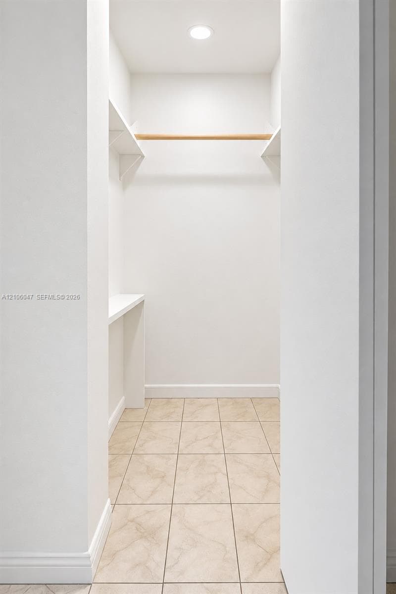 Walk-in closet featuring stone-finish tile flooring, recessed ceiling lighting, built-in shelving, and a wood-finish hanging rod