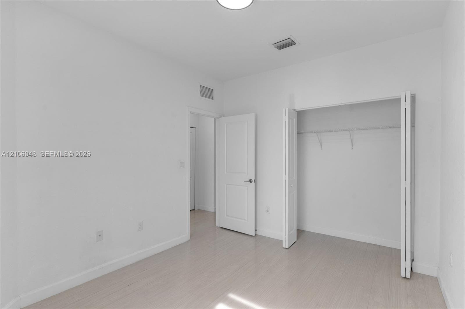 Interior space featuring light-toned wood-finish flooring, white walls, a closet with bifold doors, and a solid-core interior door