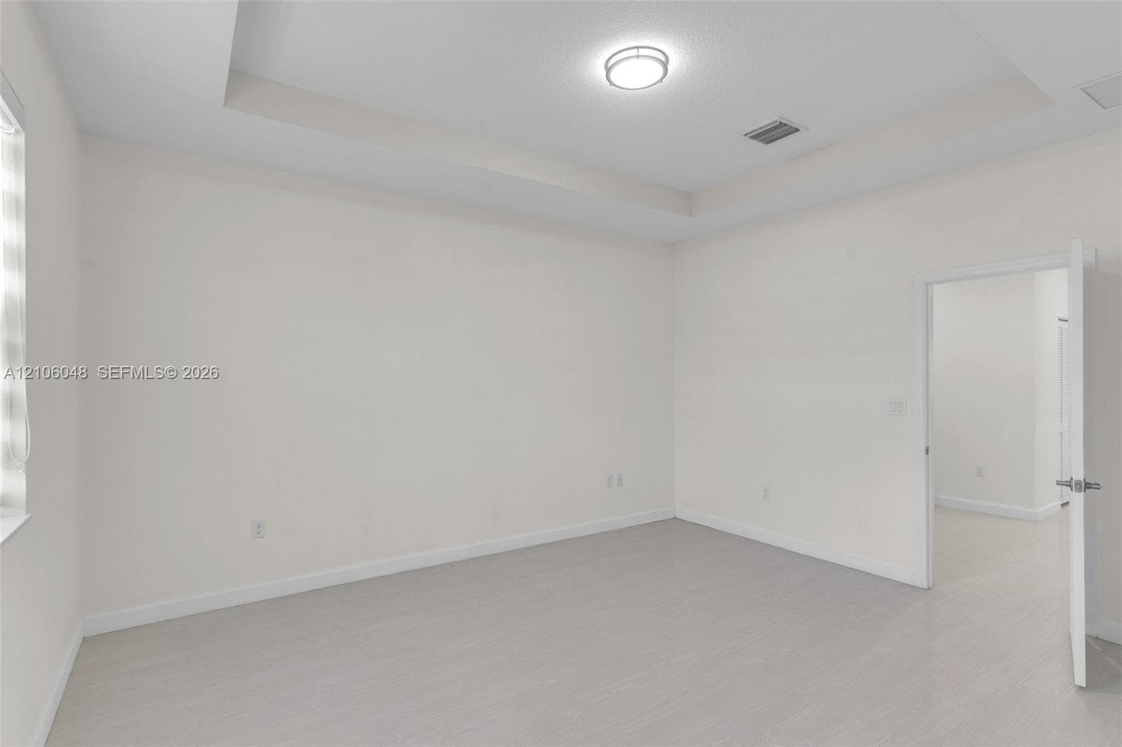 Tray ceiling featuring a central flush-mount light fixture and wood-finish flooring