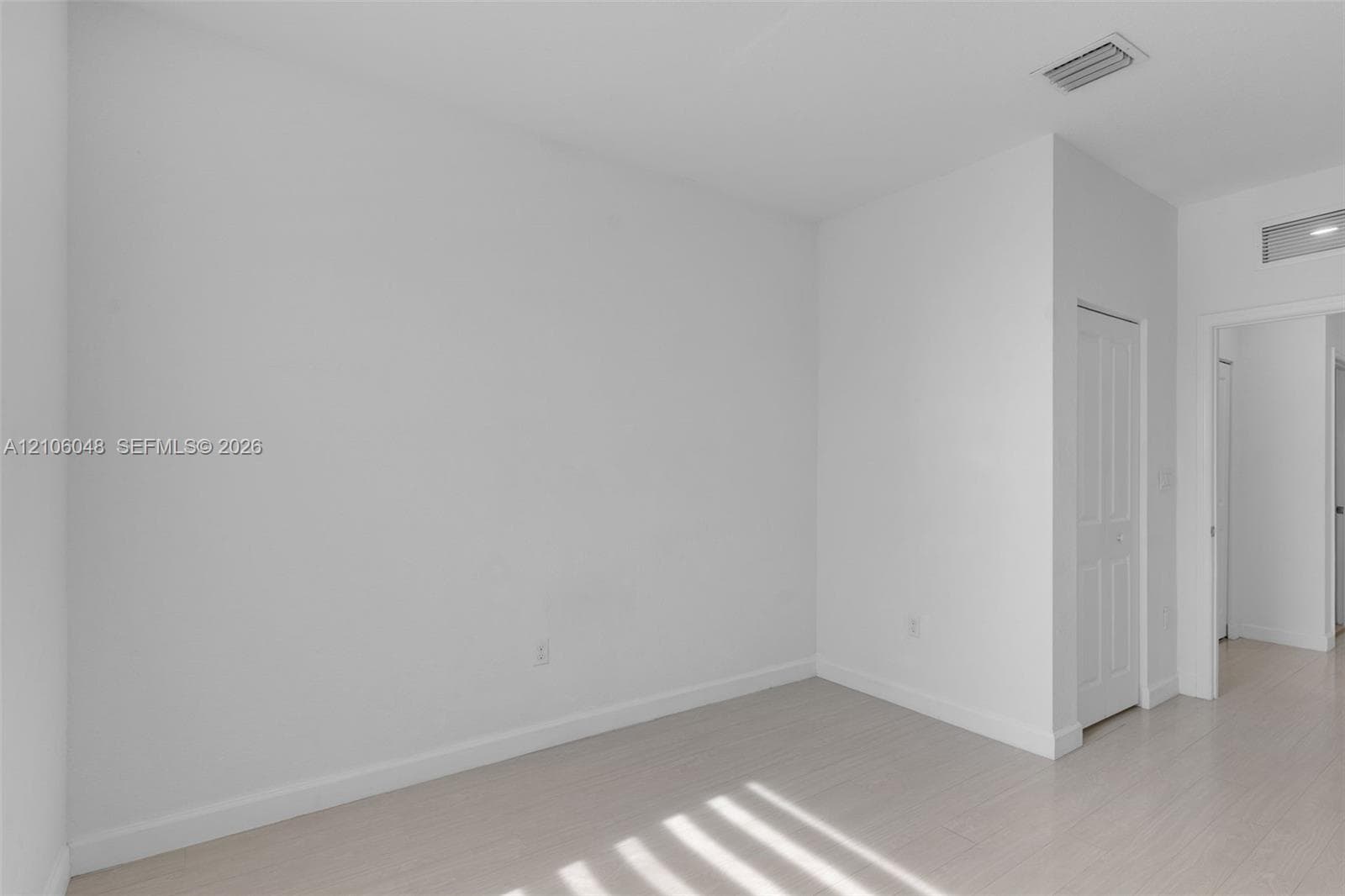 Neutral-toned interior space featuring light wood-finish flooring, smooth wall surfaces, and a multi-panel interior door