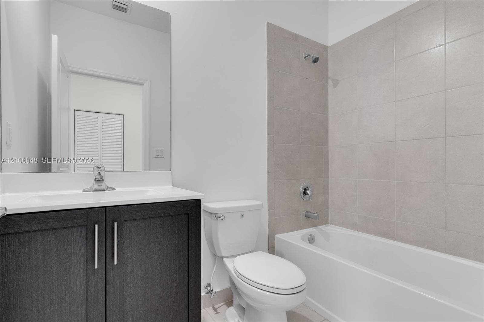 Dark-finish vanity cabinet with a light-toned countertop, large-format mirror, and bathtub with floor-to-ceiling neutral tile surround
