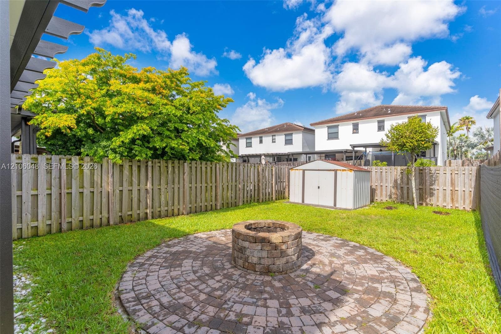Backyard featuring a circular paver patio, stone-finish fire pit, wood privacy fencing, and metal storage shed