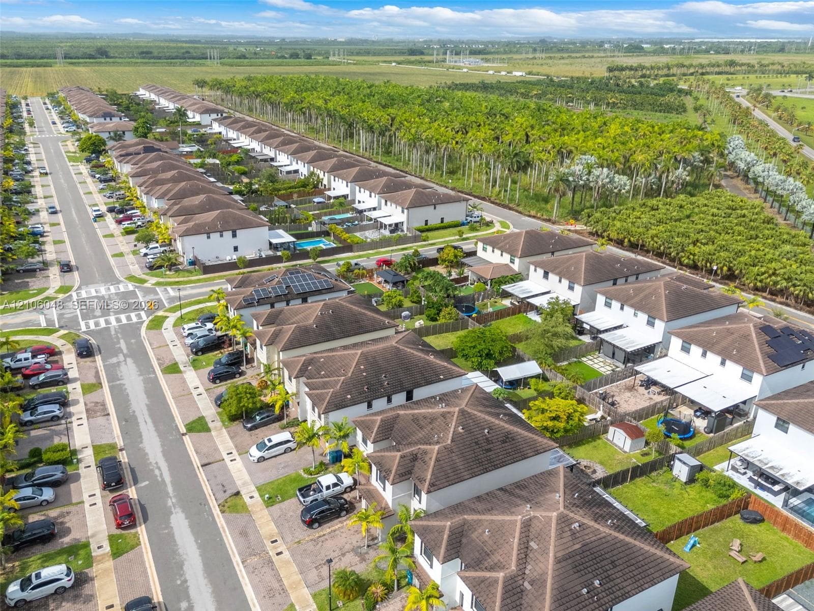 Aerial perspective of a planned community featuring multi-level residential structures, shingle rooflines, integrated solar energy panels, paved thoroughfares, and bordering natural vegetation