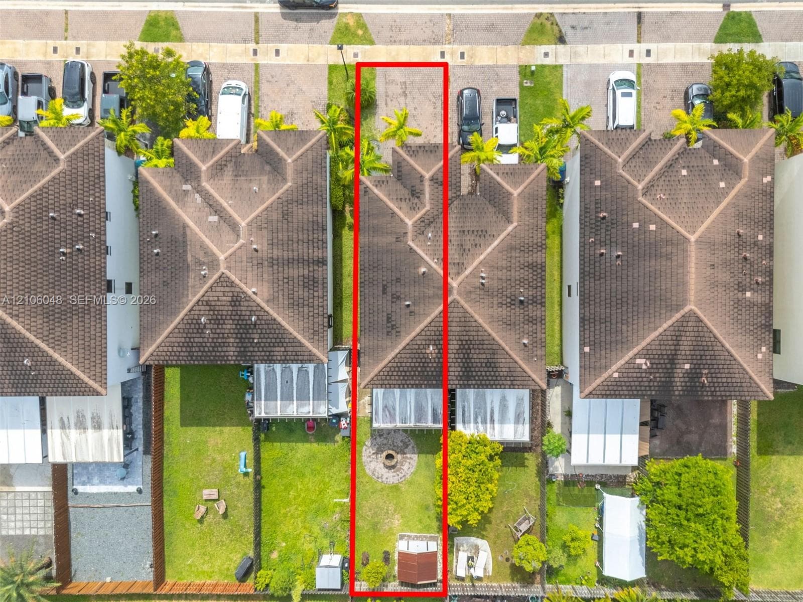 Aerial perspective of a detached residential property featuring a hipped roof, a screened-in rear patio, a stone-paved fire pit area, and a fenced backyard