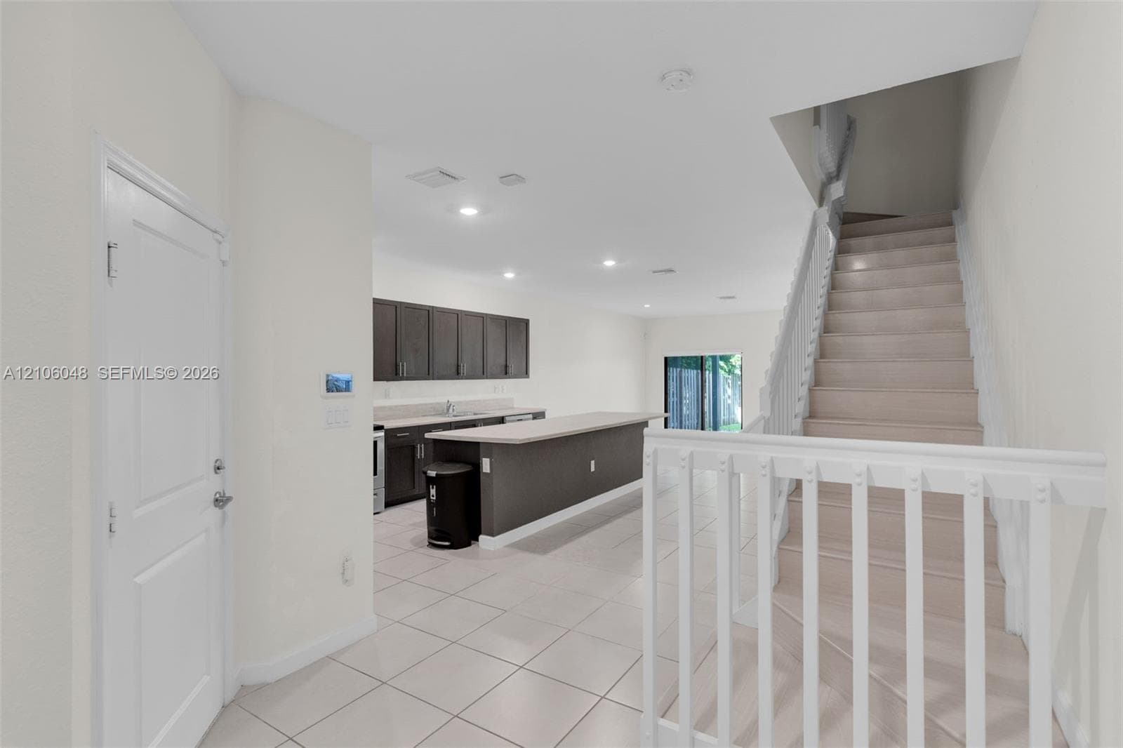 Kitchen featuring dark cabinetry, expansive countertop, and recessed lighting, complemented by tile flooring and white baluster staircase railing