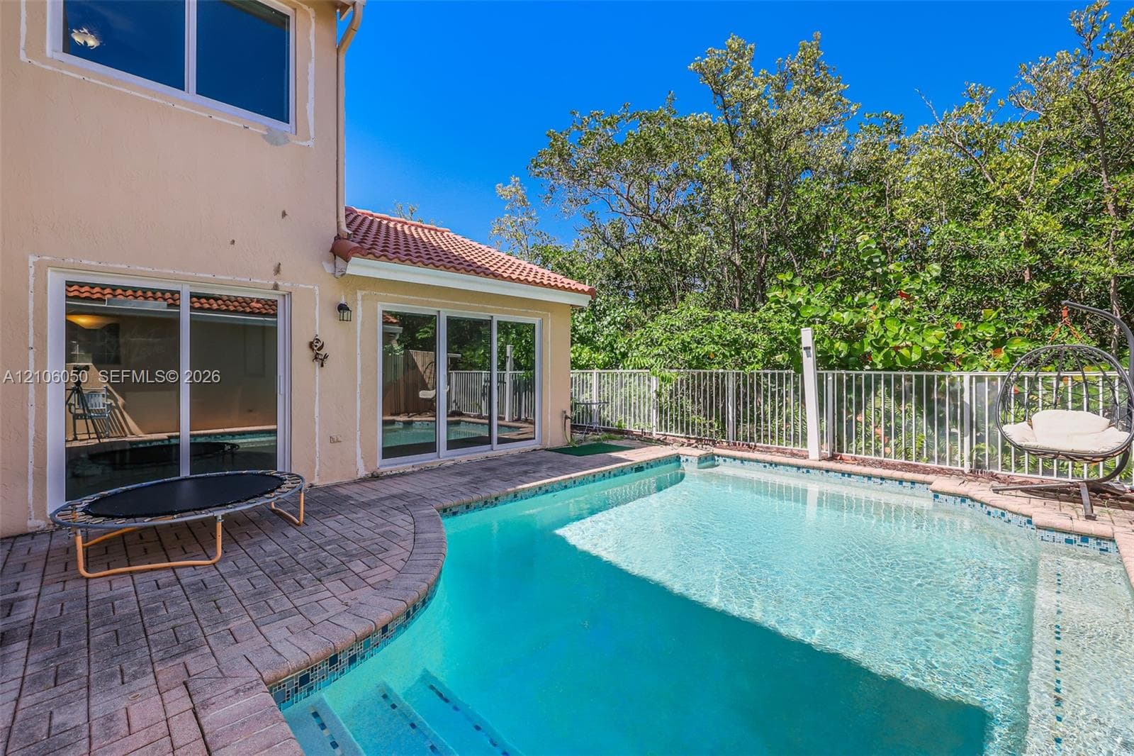 Backyard featuring an in-ground pool with built-in stairs, paver stone decking, and white metal fencing