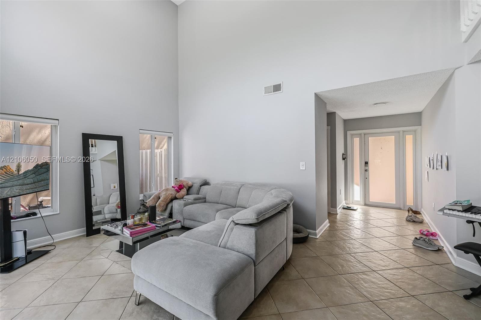 High-ceilinged room featuring ceramic tile flooring, dual windows, and an entryway with a glass-panel door and sidelights