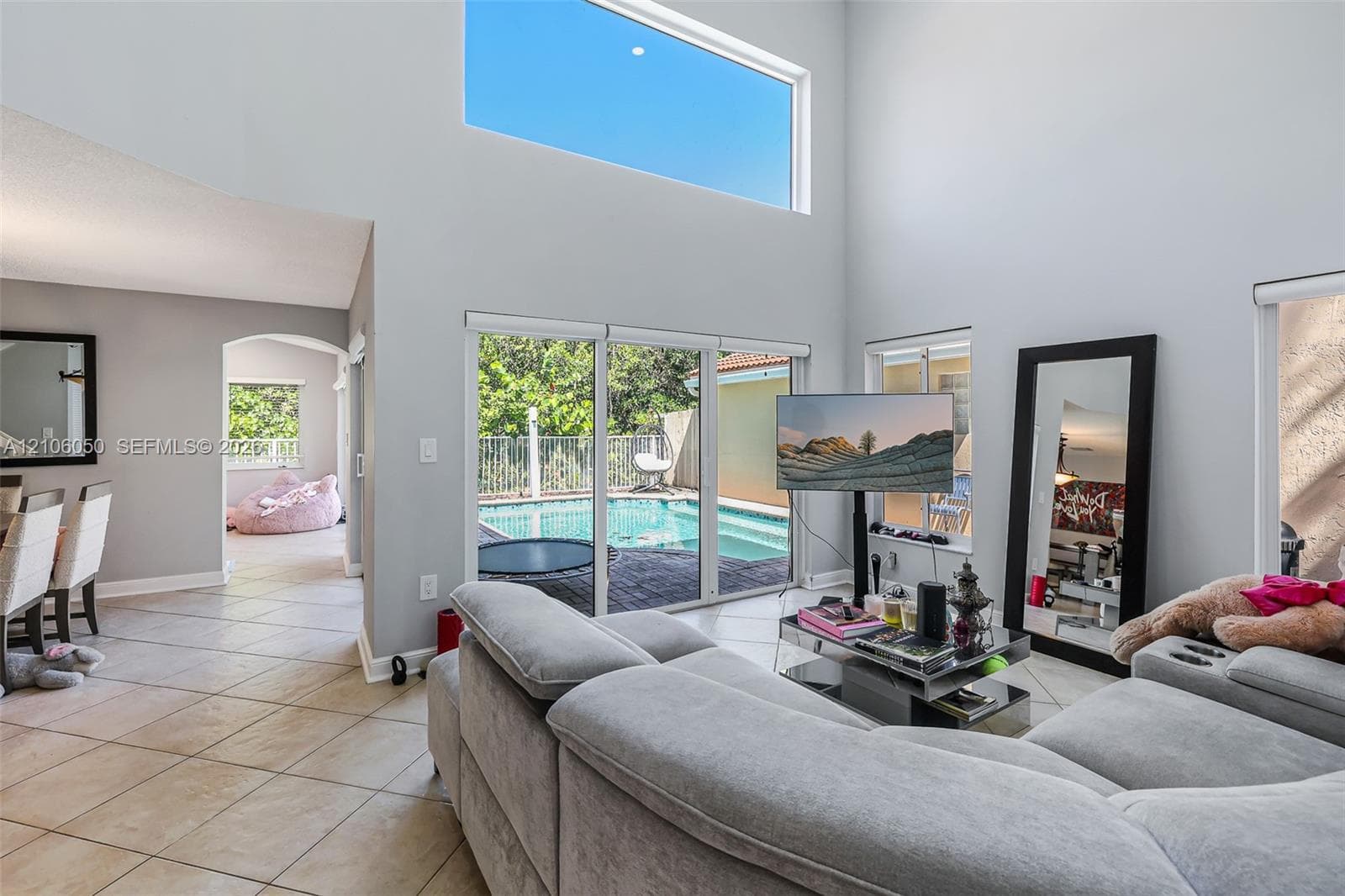 Double-height ceiling with clerestory windows, tile flooring, and oversized sliding glass doors opening to a screened pool enclosure