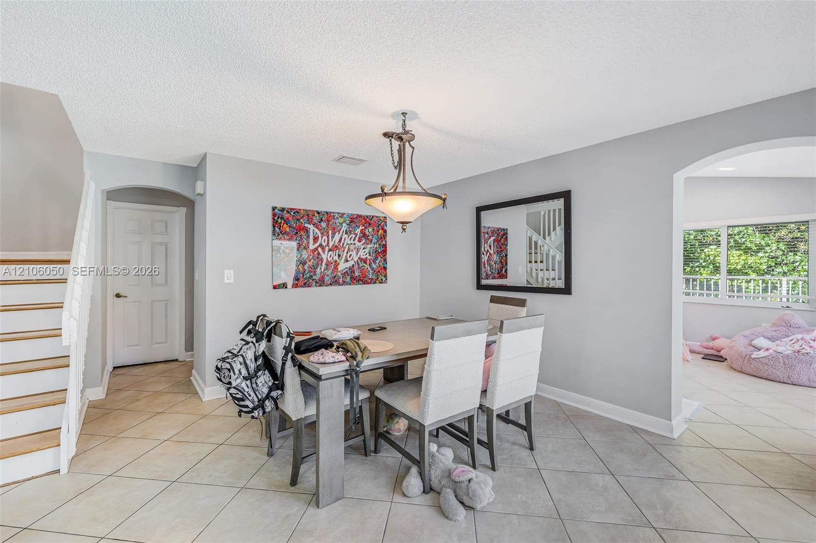 Dining space featuring neutral tile flooring, arched entryways, a central metal pendant light fixture, and stairs with wood treads