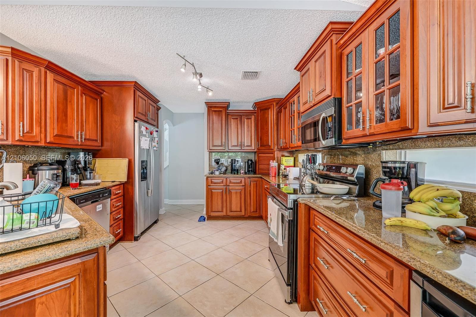 Kitchen featuring stained wood cabinetry with glass-panel upper doors, stone-finish countertops, stainless steel appliances, and ceramic tile flooring