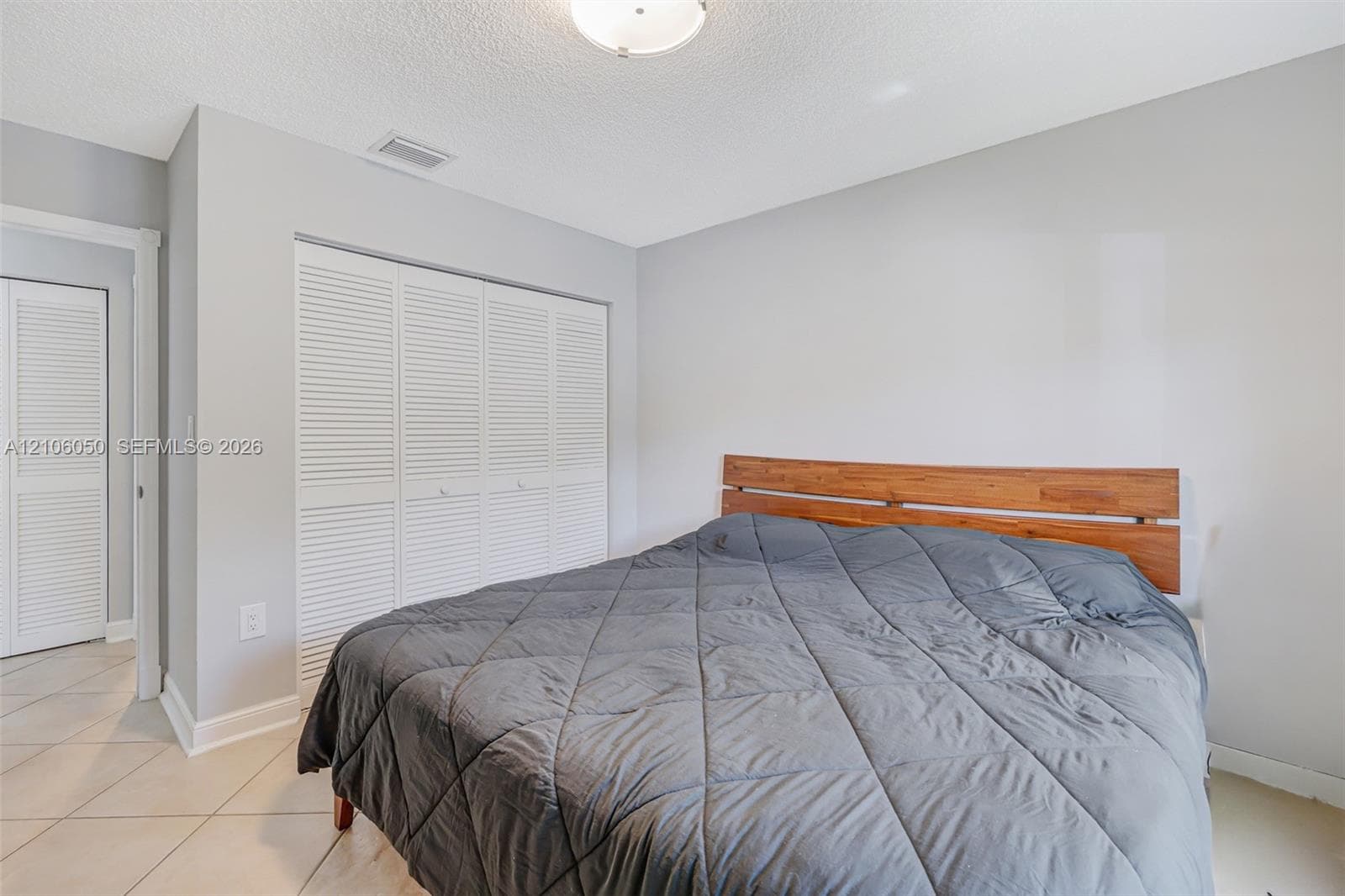 Neutral-toned interior featuring louvered closet doors, tile flooring, and a flush-mount ceiling light fixture