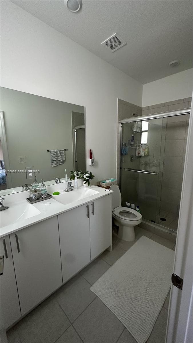 Double-sink vanity with white cabinetry, light-toned solid surface countertop, full-width mirror, and a walk-in shower featuring sliding glass doors and tiled wall surrounds