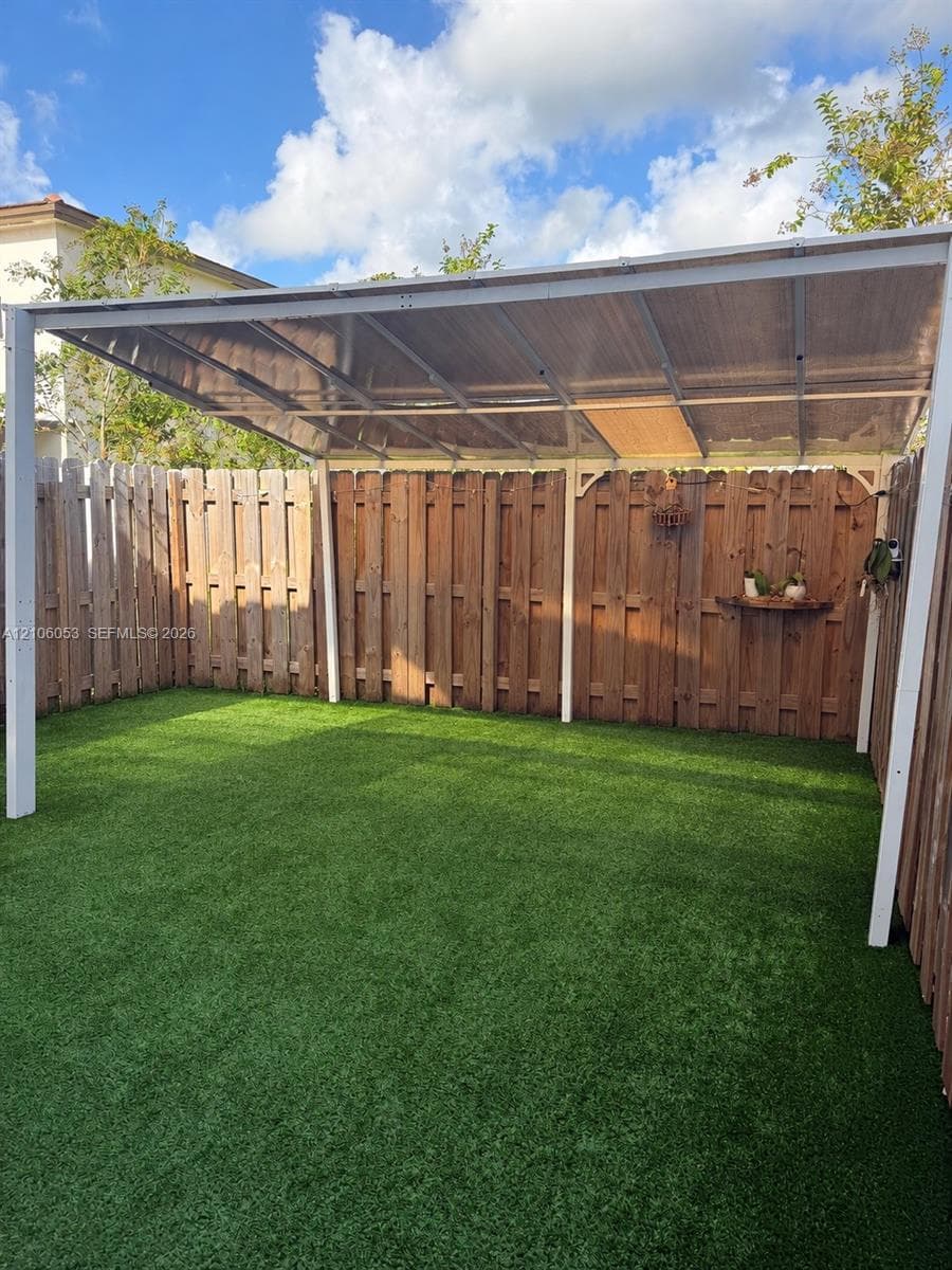 Enclosed backyard featuring a synthetic lawn, perimeter wood fencing, and a metal-framed covered patio structure