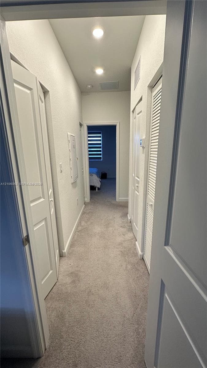 Hallway featuring neutral carpeting, recessed ceiling lighting, and multiple interior doors, including a louvered closet door