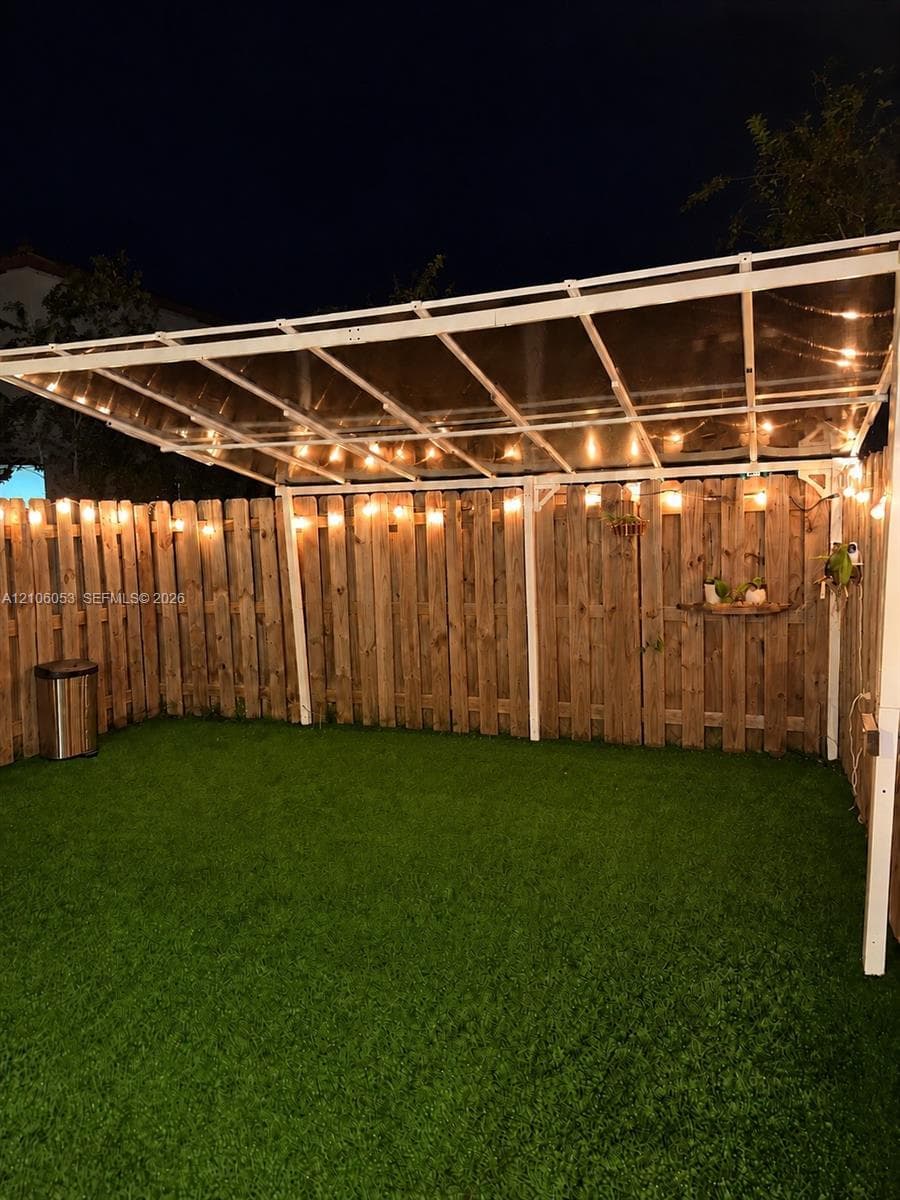 Outdoor area featuring a synthetic turf lawn, wood privacy fencing, and a white metal-frame patio cover with a translucent canopy