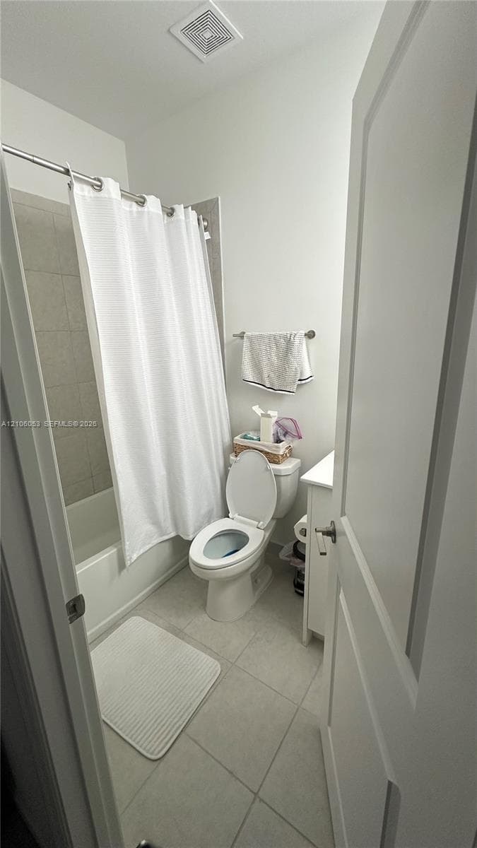 Bathroom featuring light-toned tile flooring, a combination tub and shower with tile surround, a white pedestal vanity, and a standard-height toilet
