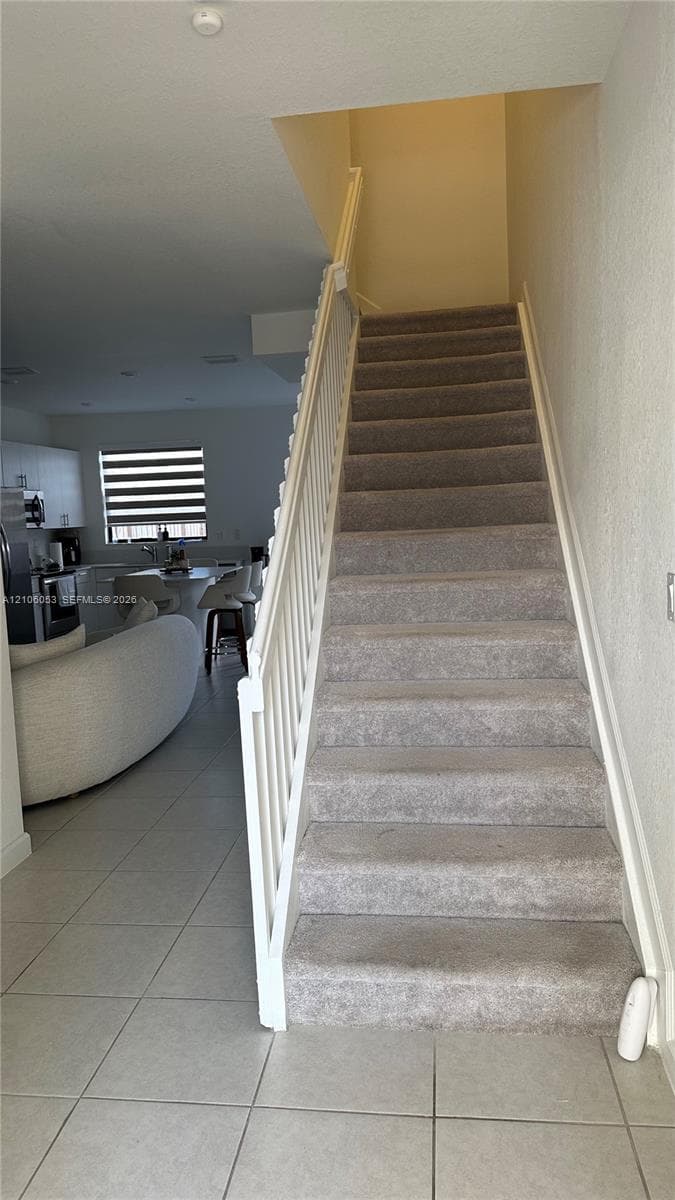Staircase featuring carpeted treads and a white wooden balustrade, paired with light-toned tile flooring
