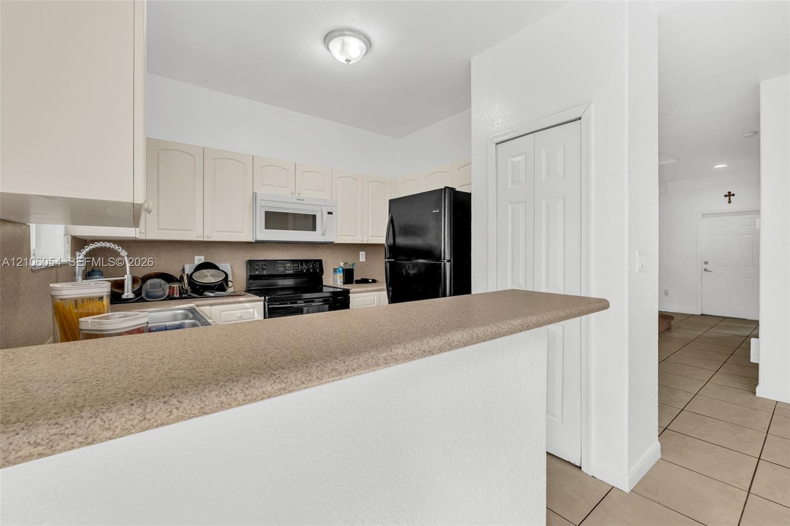 Kitchen featuring off-white cabinetry, solid-surface countertops, black built-in appliances, a dual-basin sink with a gooseneck faucet, and tiled flooring