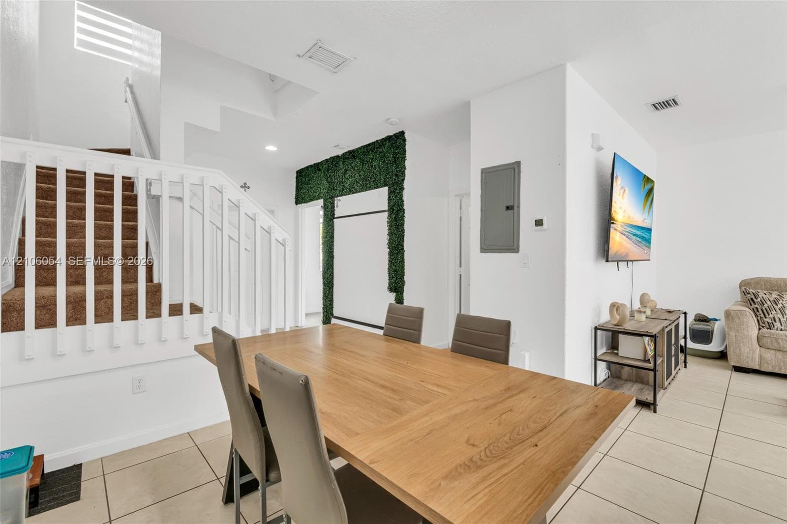 Open-concept interior featuring large-format tile flooring, a white wooden staircase railing, and a decorative greenery-accented wall feature