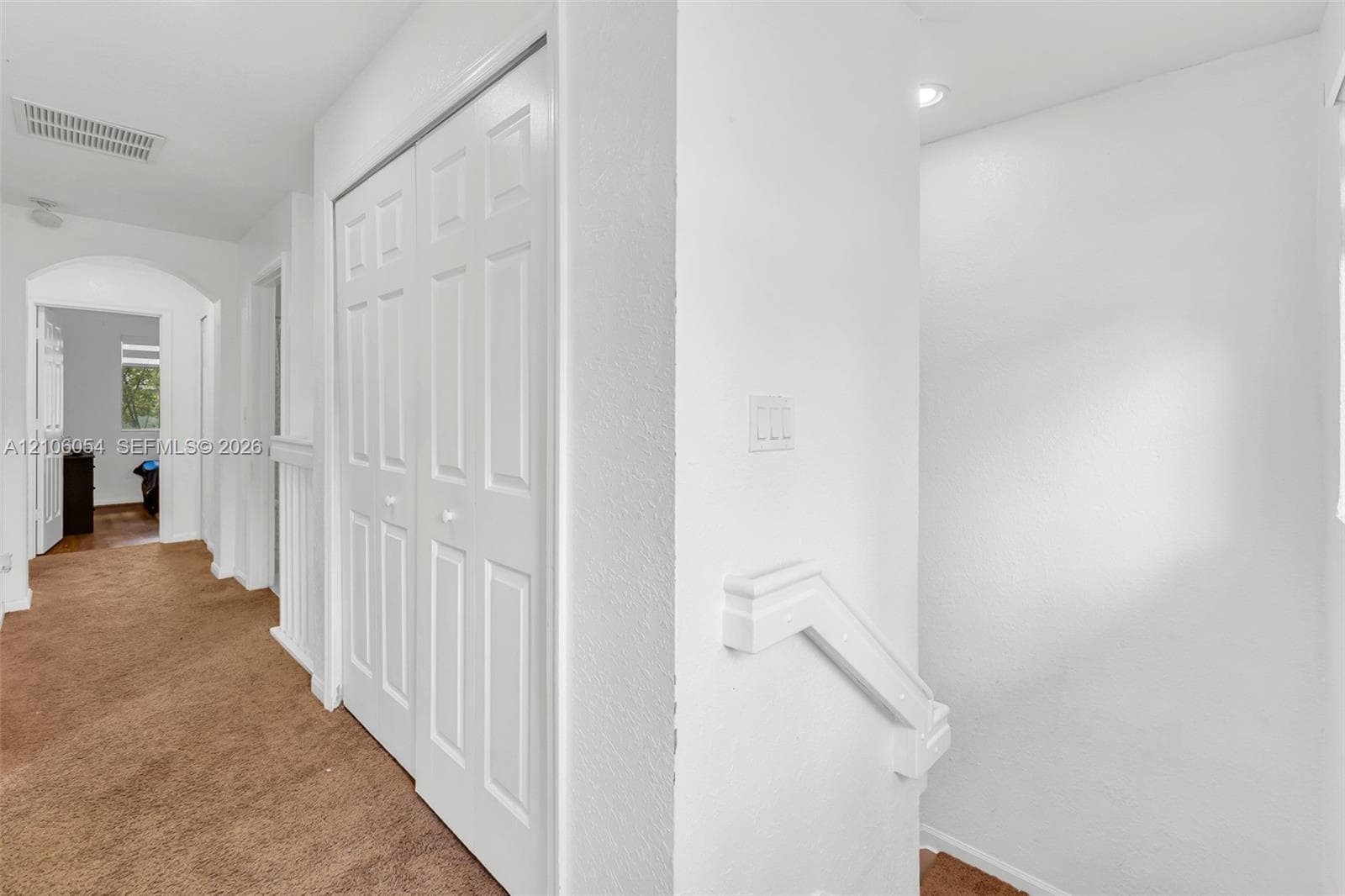 Hallway featuring carpeted flooring, a recessed ceiling light, white bifold closet doors, and a staircase with a white handrail
