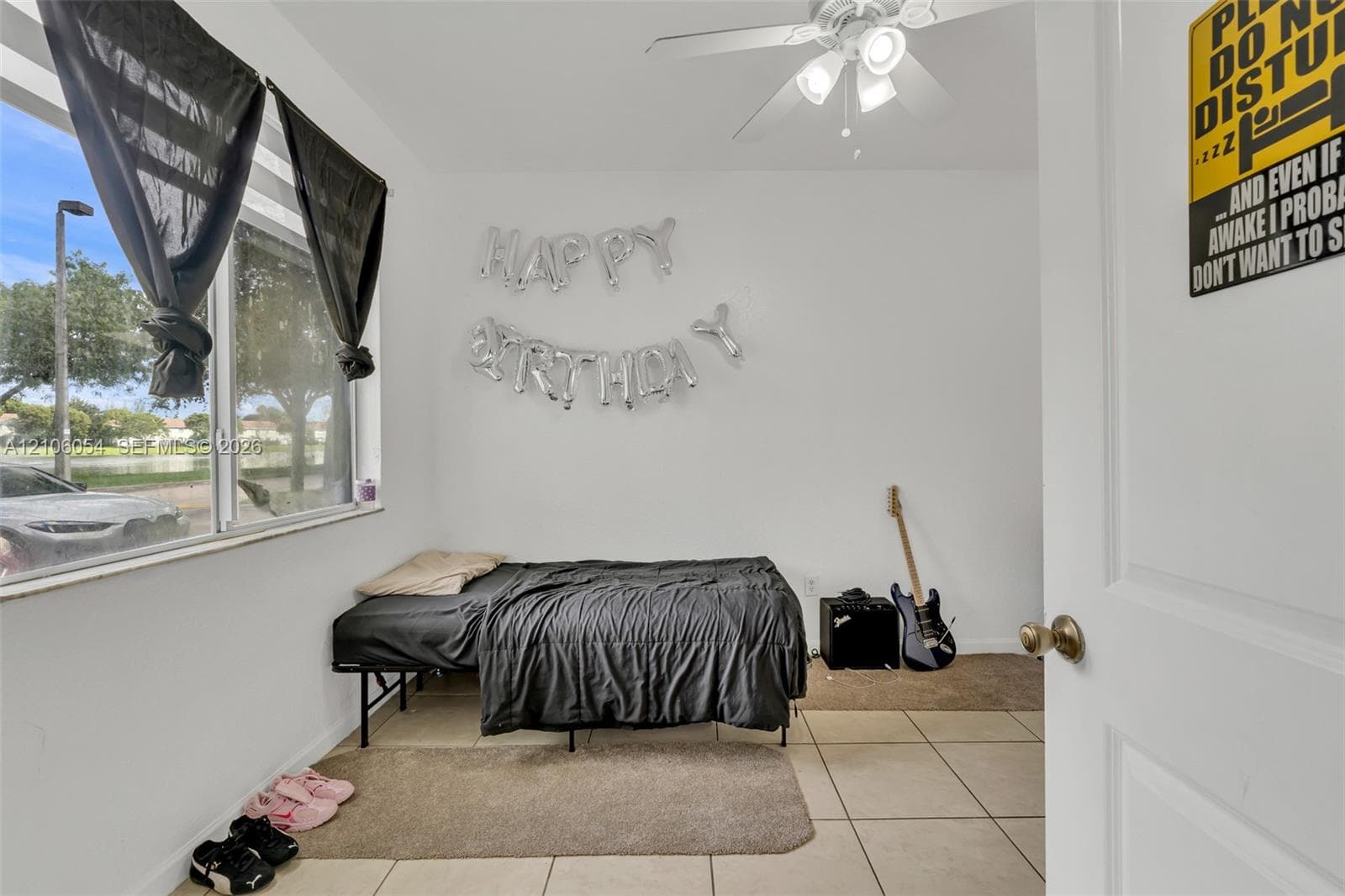 Large window with exterior water feature backdrop, neutral tile flooring, and white ceiling fan with three-light fixture