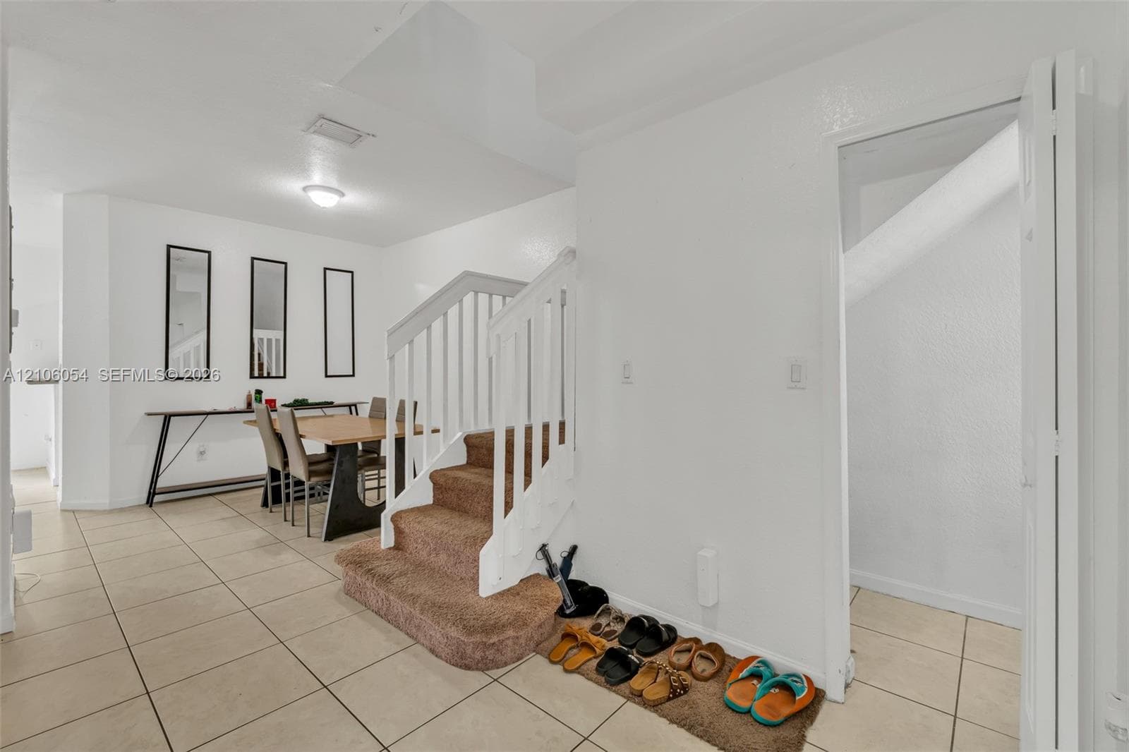 Staircase featuring a white balustrade, neutral carpeting, and tile flooring throughout the area