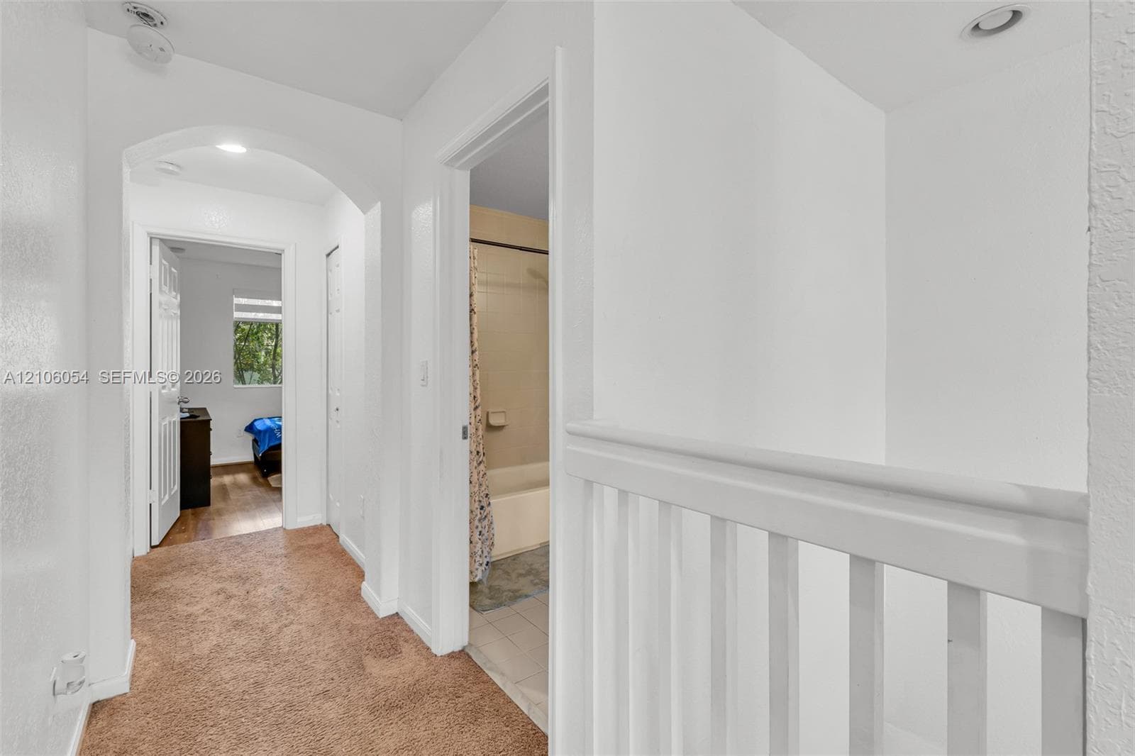 Interior hallway featuring a white arched architectural detail, recessed lighting, and a painted wooden staircase railing