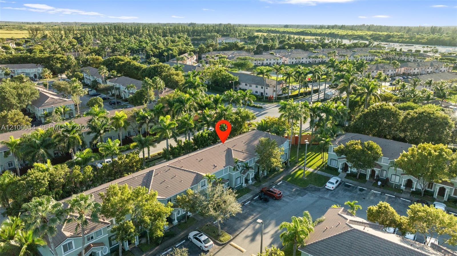 Aerial perspective of a multi-unit residential complex featuring gabled tile roofing, stucco exterior cladding, paved surface parking, and mature palm tree landscaping