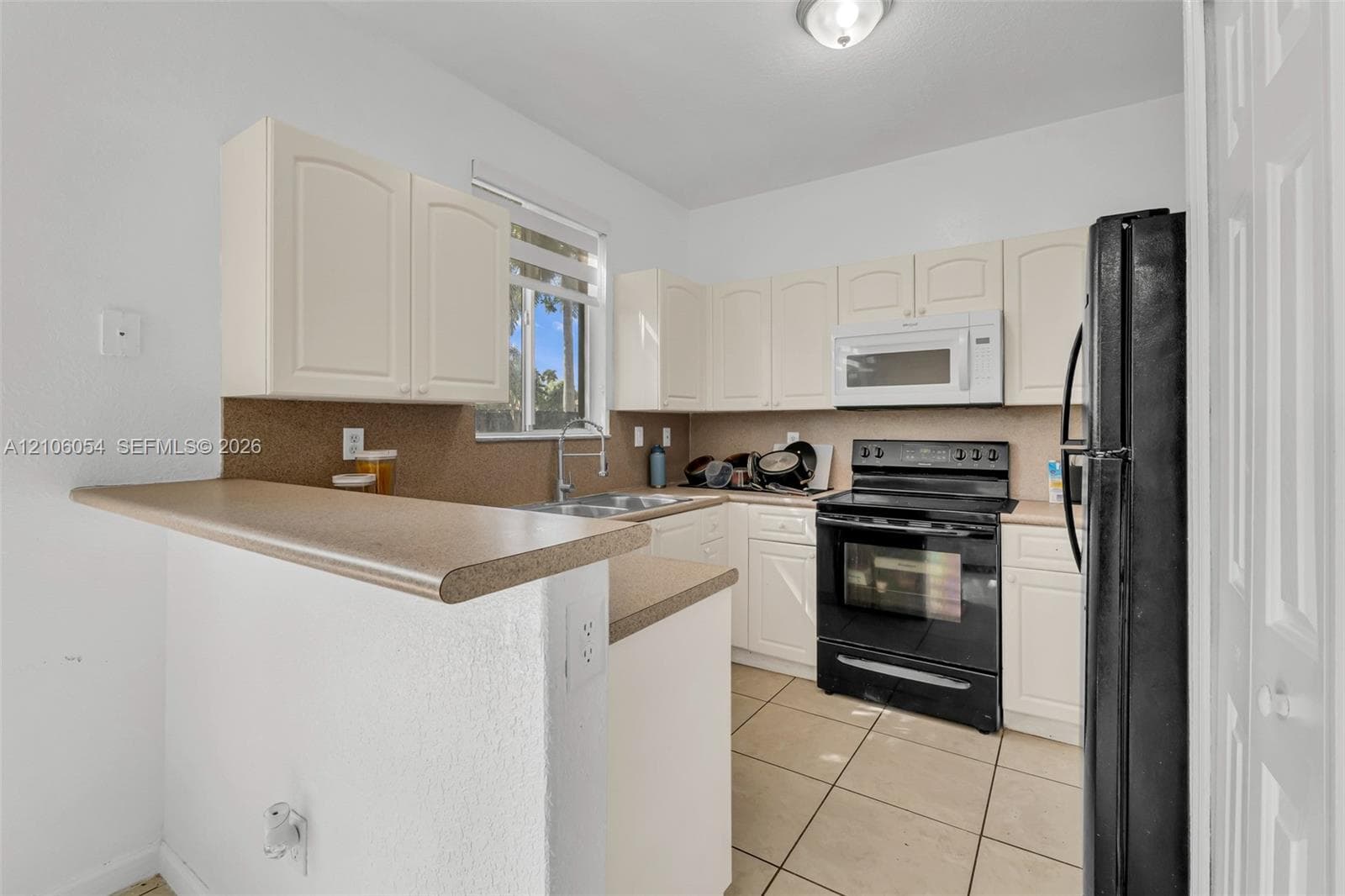 Kitchen featuring white cabinetry, solid-surface countertops, tile flooring, and integrated black appliances