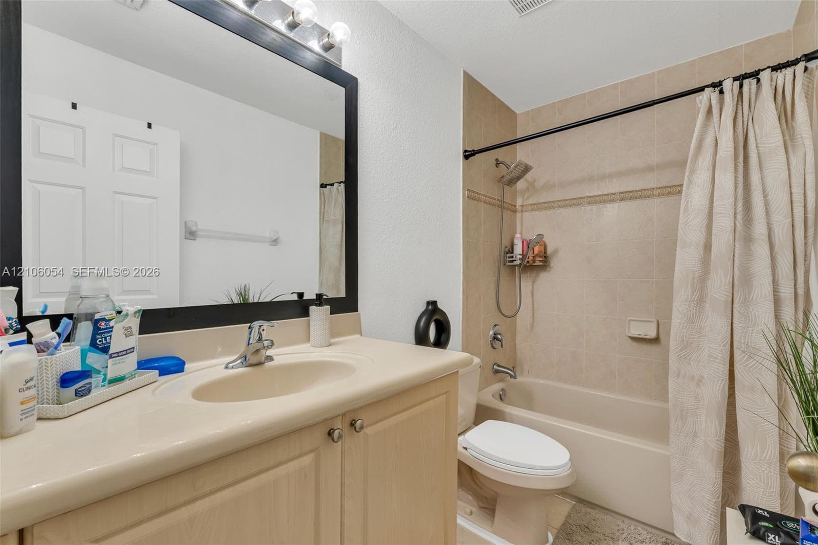 Bathroom featuring a vanity with integrated sink, large-format mirror with dark frame, wall-mounted light fixture, and a tub-shower combination with tiled surround