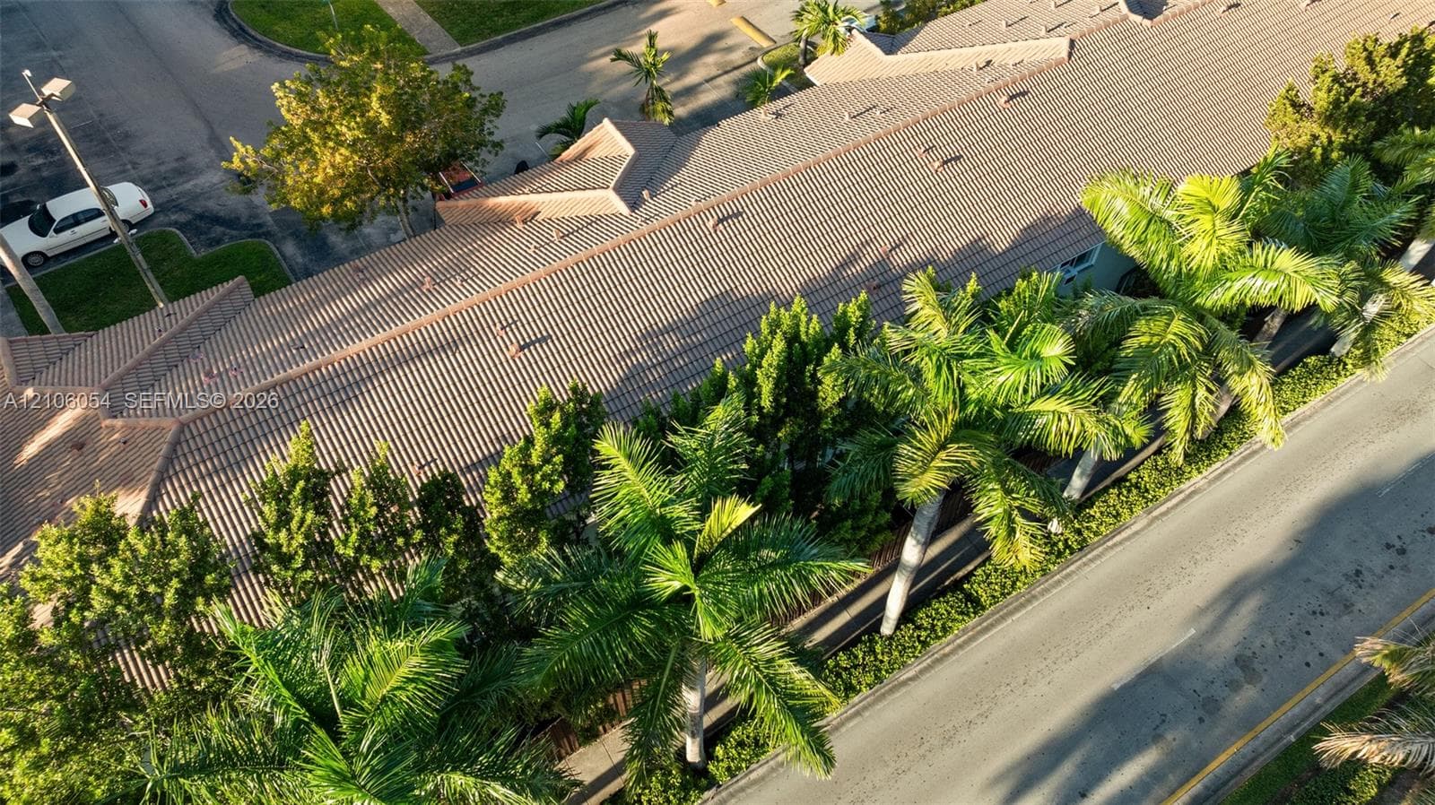 Aerial view featuring a multi-gabled tiled roof structure surrounded by mature palm trees and established landscaping