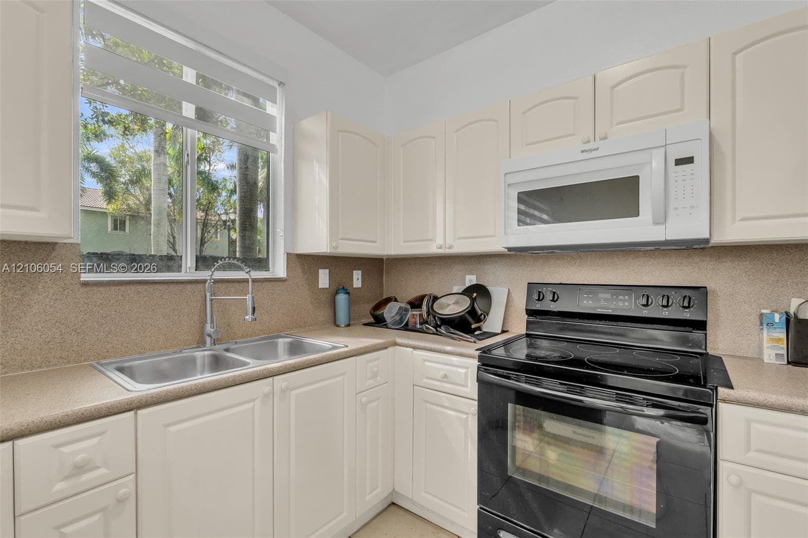Kitchen featuring white cabinetry, solid-surface countertops, dual-basin stainless steel sink with pull-down faucet, and integrated black electric range and microwave