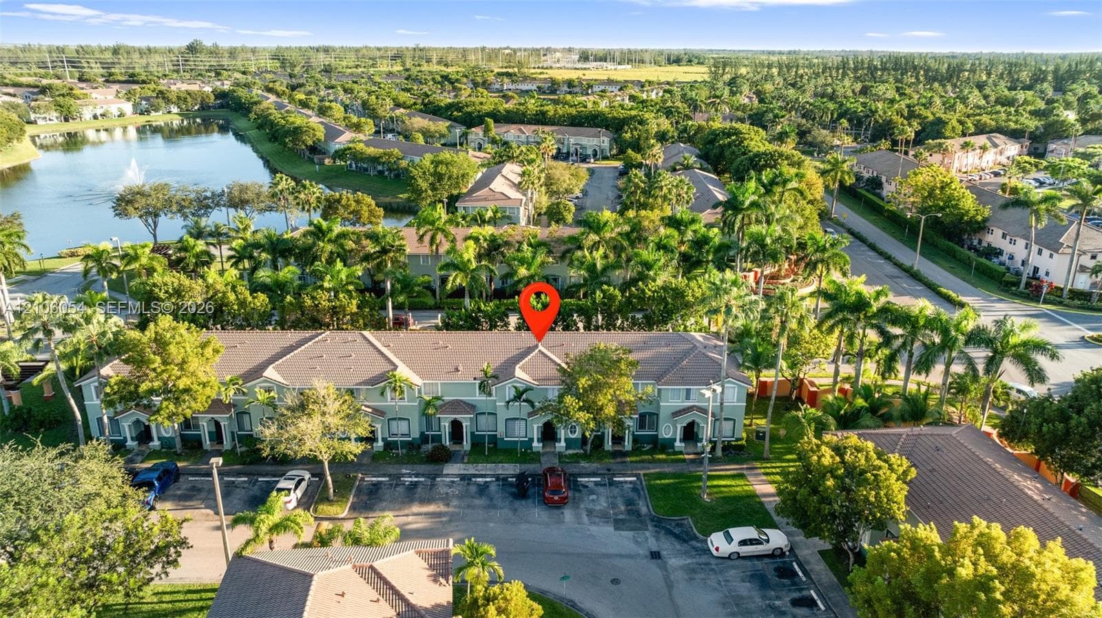 Multi-story residential structure featuring a hip roof, stucco exterior, paved parking area, and mature palm landscaping