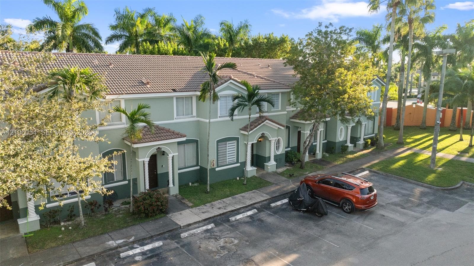 Multi-level exterior featuring a two-tone facade, tile roof, arched entryway details, and paved surface parking