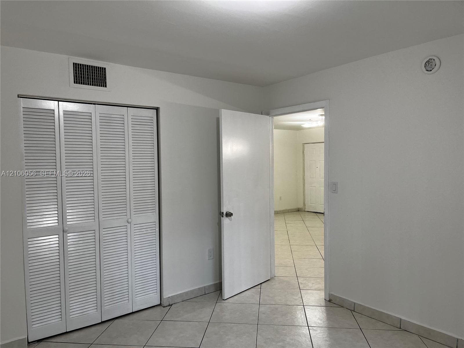 Neutral-toned tile flooring, white interior doors, and a four-panel louvered closet door
