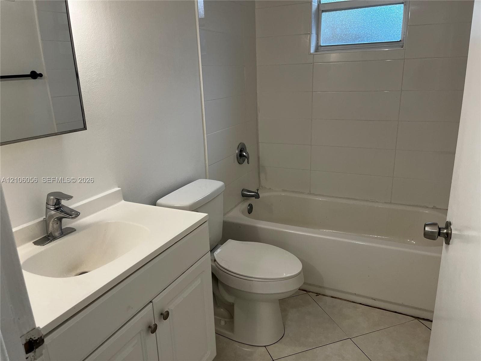 Bathroom featuring a white vanity cabinet with an integrated basin, chrome finish faucet, tiled tub surround, and ceramic tile flooring