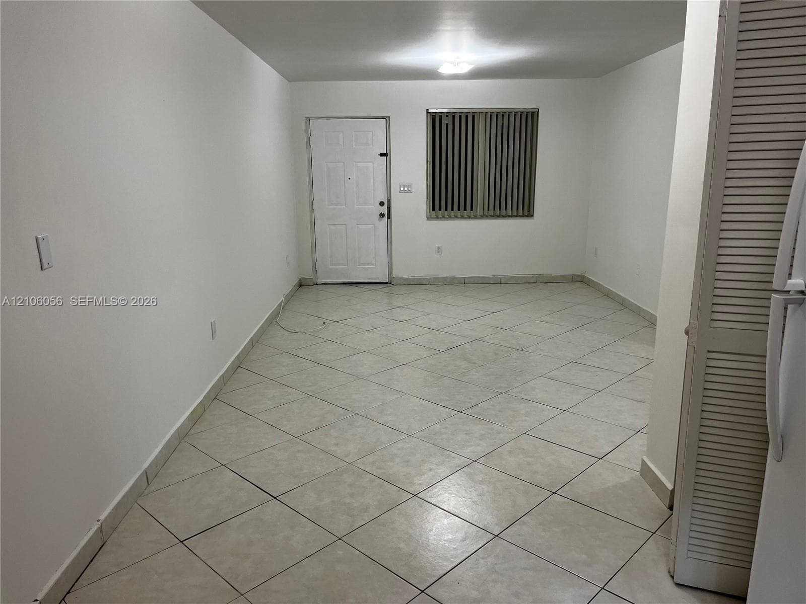 Interior space featuring diagonal tile flooring, a multi-panel entry door, and vertical window blinds