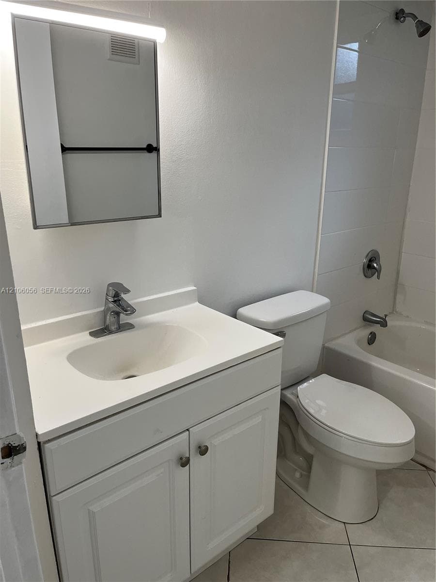 Bathroom featuring a vanity with integrated sink and chrome faucet, lighted medicine cabinet, white toilet, and tub-shower combination with tiled surround