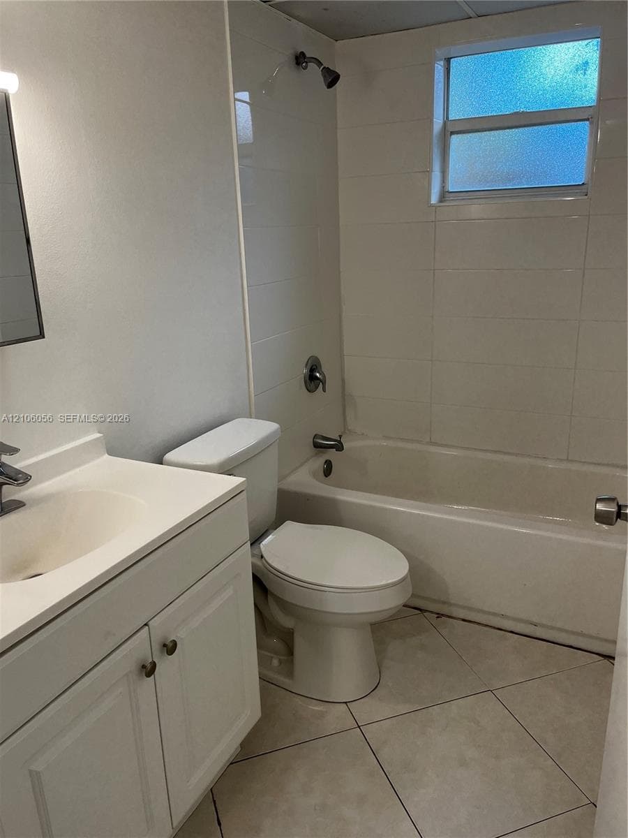 Bathroom featuring a vanity with a drop-in sink, large-format tile flooring, a shower-tub combination with tiled surround, and an obscured-glass window