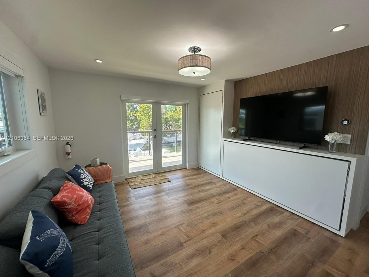 Wood-finish flooring, built-in cabinetry with integrated wall paneling, recessed lighting, drum-style flush mount ceiling fixture, and glass-paned double doors