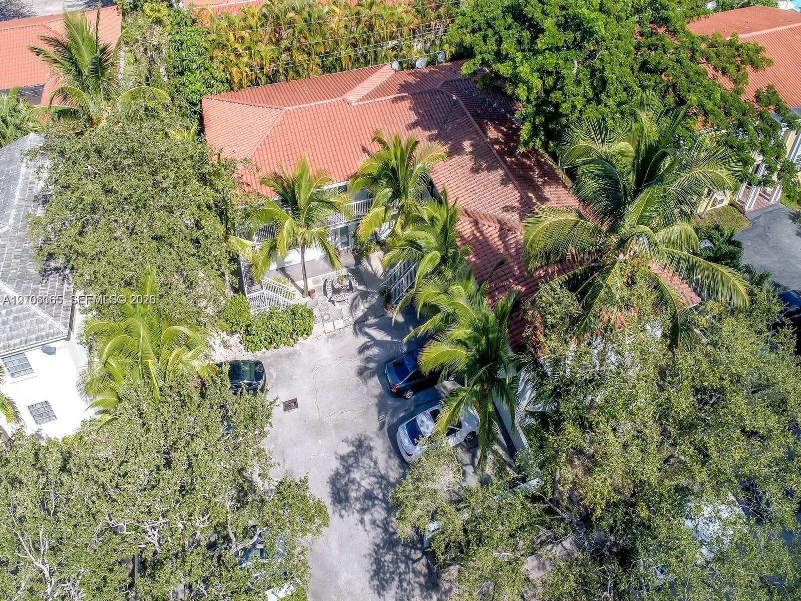 Exterior structure featuring a red tile roof, concrete driveway, and mature palm trees