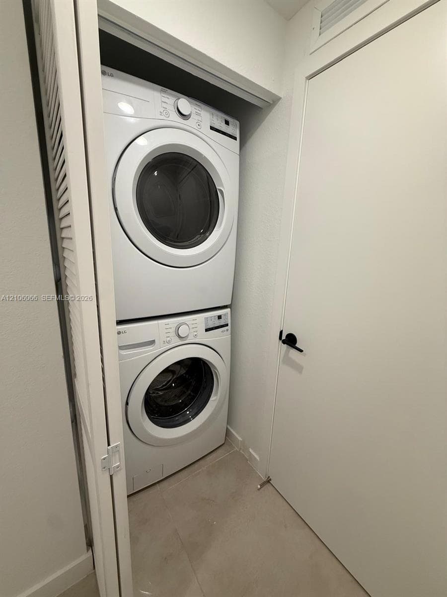 Dedicated laundry closet featuring a stackable washer and dryer, tile flooring, and a white paneled door with matte black hardware