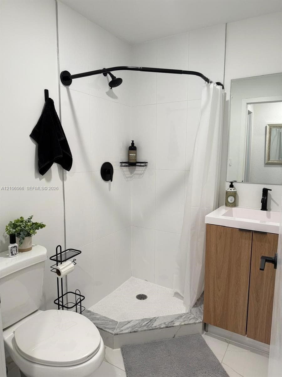 Corner shower featuring large-format white tile, stone-finish threshold, and matte black hardware including a curved shower rod and faucet